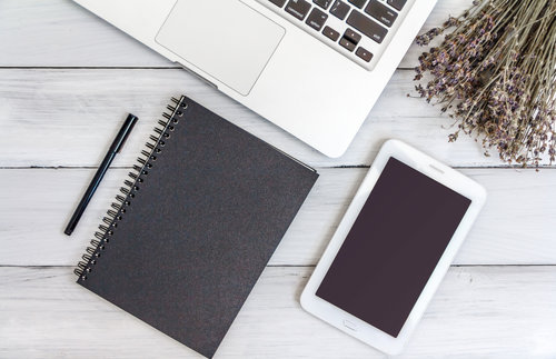 White office desk with laptop, smartphone, notebook on wooden table. Top view with copy space. Student or business accessories flatlay. Office supplies and gadgets on background. View from above.